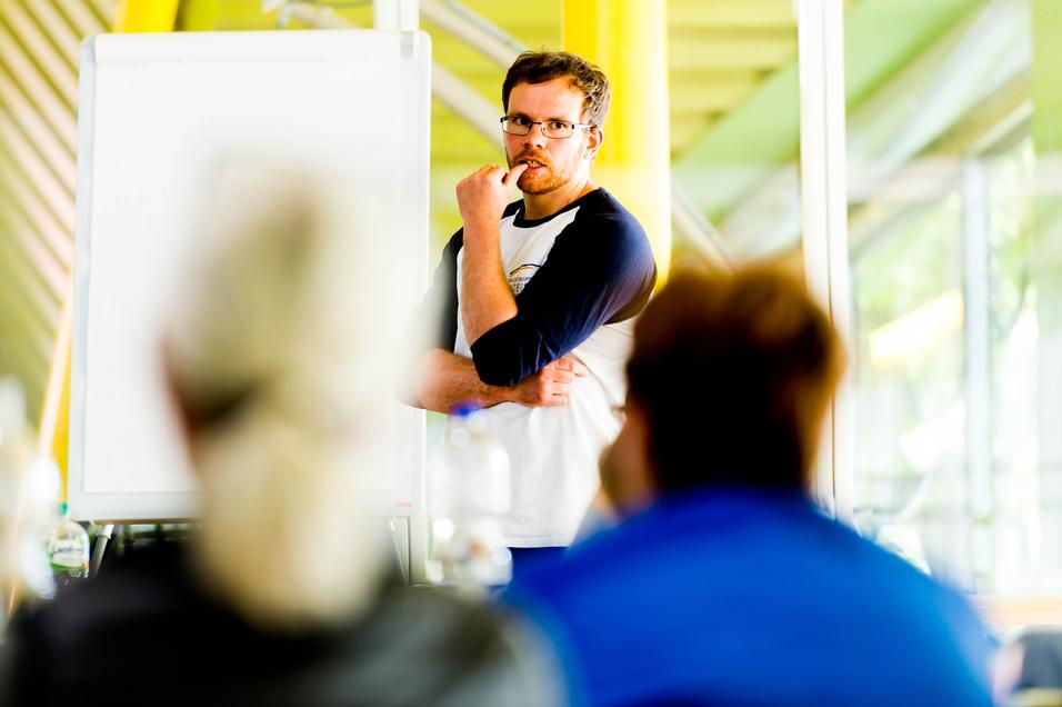 Mann mit Brille spricht vor einer Gruppe, ein Flipchart ist im Hintergrund sichtbar.