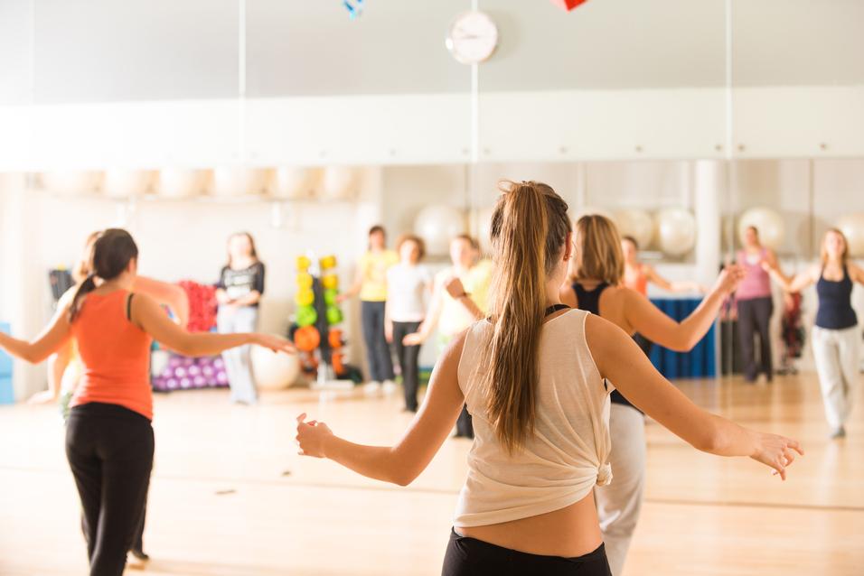 Gruppe von Frauen in Sportkleidung beim Tanztraining in einem gut beleuchteten Fitnessraum mit Spiegeln.